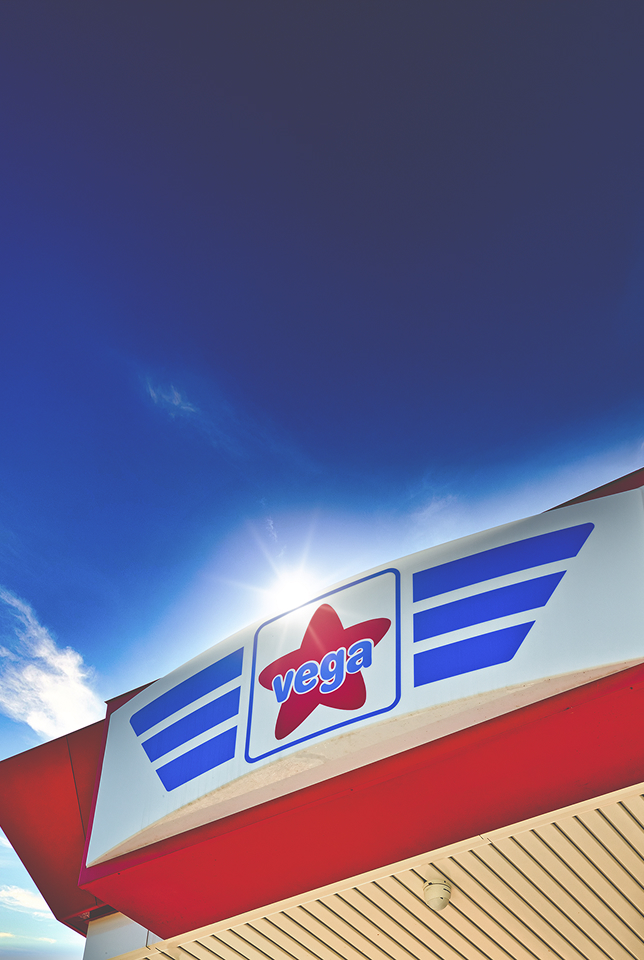 Insegna della stazione di servizio Vega Carburanti con logo sotto un cielo azzurro soleggiato